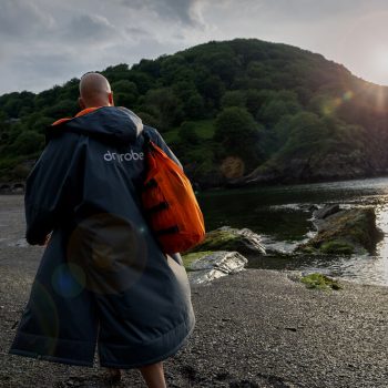 What is a Dryrobe and your FAQ Answers Revealed. Man walking near water wearing a grey and orange Dryrobe.