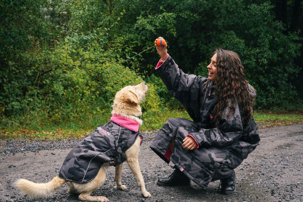 Are Dryrobes good for dog walking? Woman giving her dog a treat while on a dog walk and wearing her pink and black camo Dryrobe.
