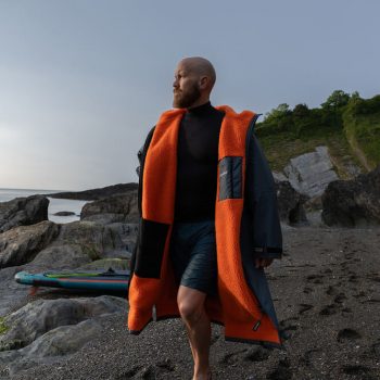 How to wash a Dryrobe and other cleaning and care instructions. Man wearing a grey and orange Dryrobe Advance on a beach.