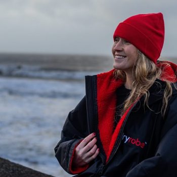 How to wear and use a Dryrobe. Girl wearing a red and black Dryrobe at the beach.